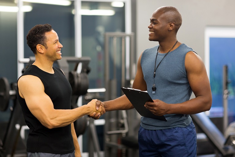 friendly african gym trainer handshaking with mid age client in gym