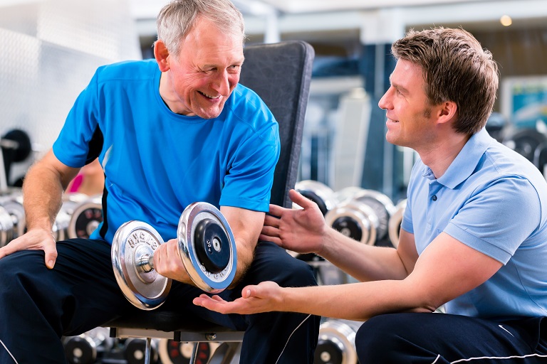 Senior man and trainer at exercise in gym with dumbbell weights